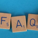 Flat lay of scrabble tiles spelling 'FAQ' with toy hands on a blue background, creating a conceptual image.
