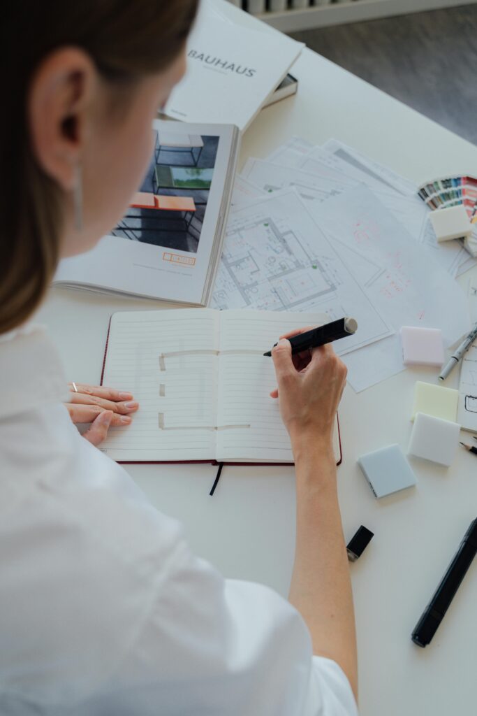 Interior designer sketching a floor plan with architecture materials on desk.